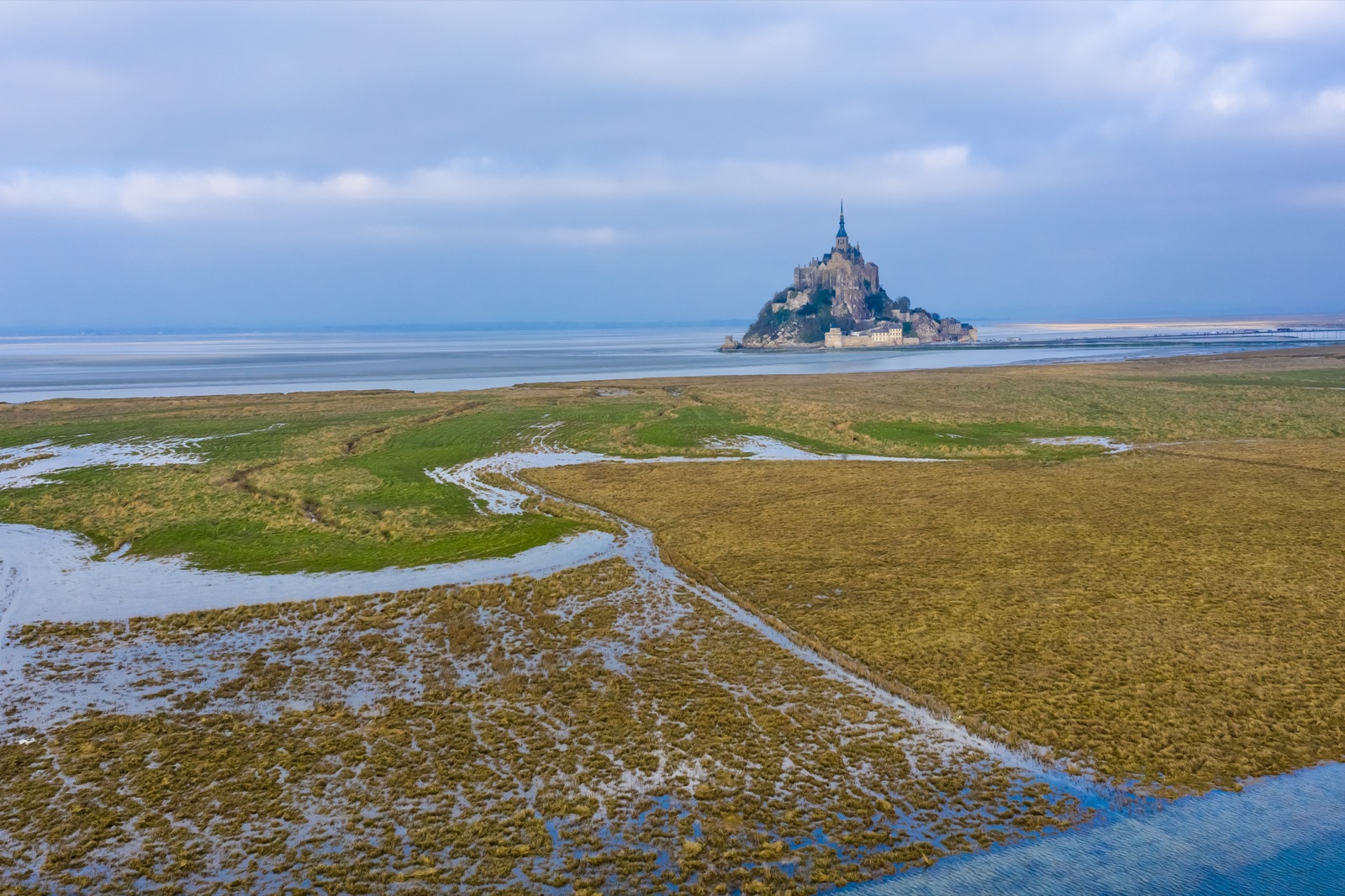 Salt meadows and tidal channels on the edge of the bay, with Mont-Saint-Michel on the horizon